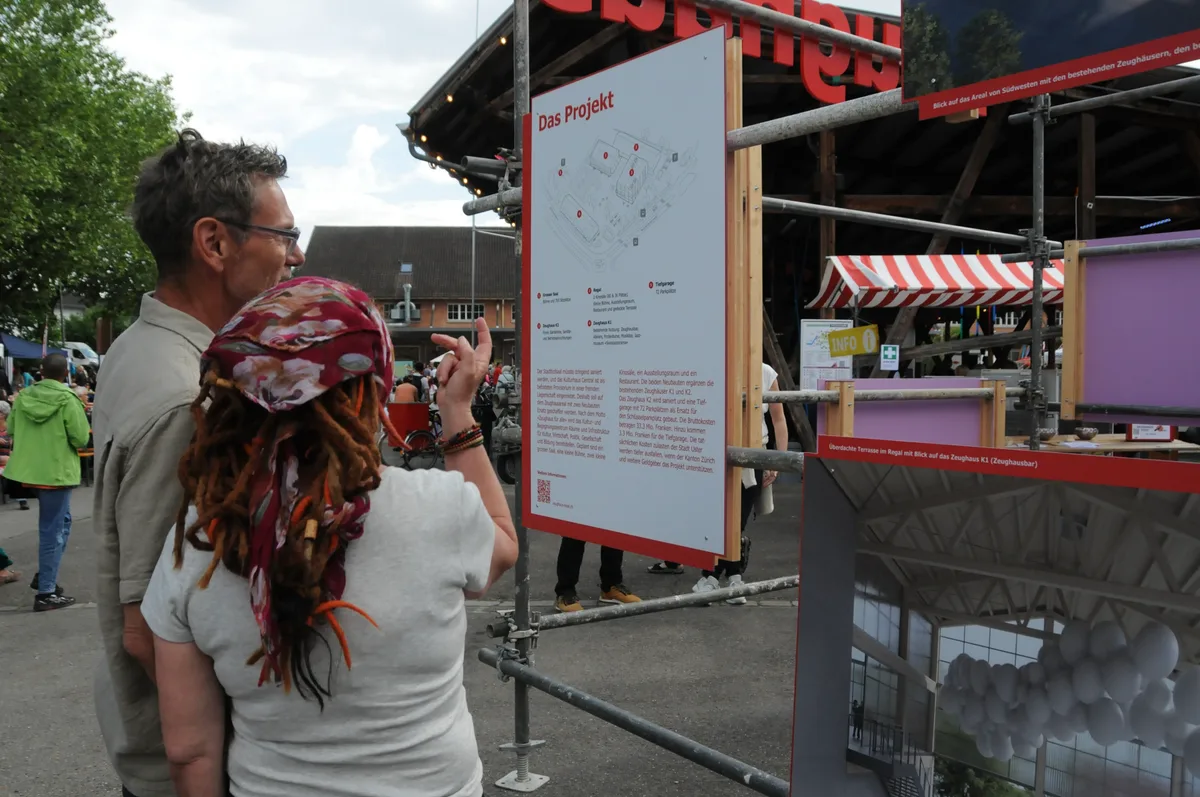 Man sieht zwei Festbesucher über das Bauprojekt diskutieren.